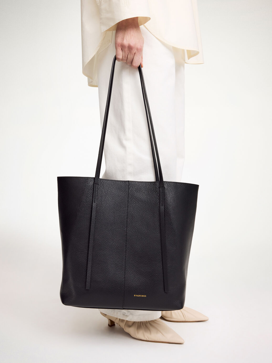 By Malene Birger Abilso veske i sort, strukturert skinn, med tote-form, liten logo i front og lange bærereimer.
