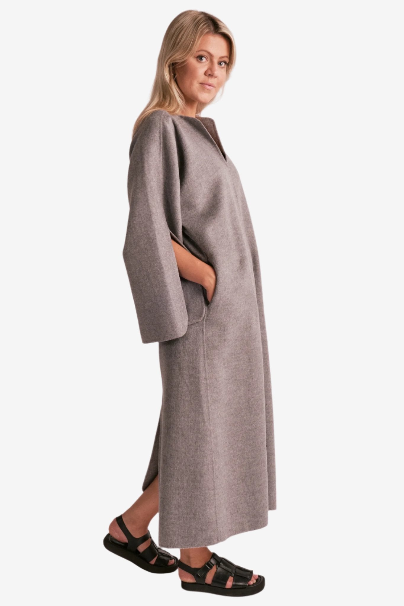 By Malene Birger Cais kjole i grått, laget av 100% ull, med en løs passform, v-utringning og splitt på ermene.