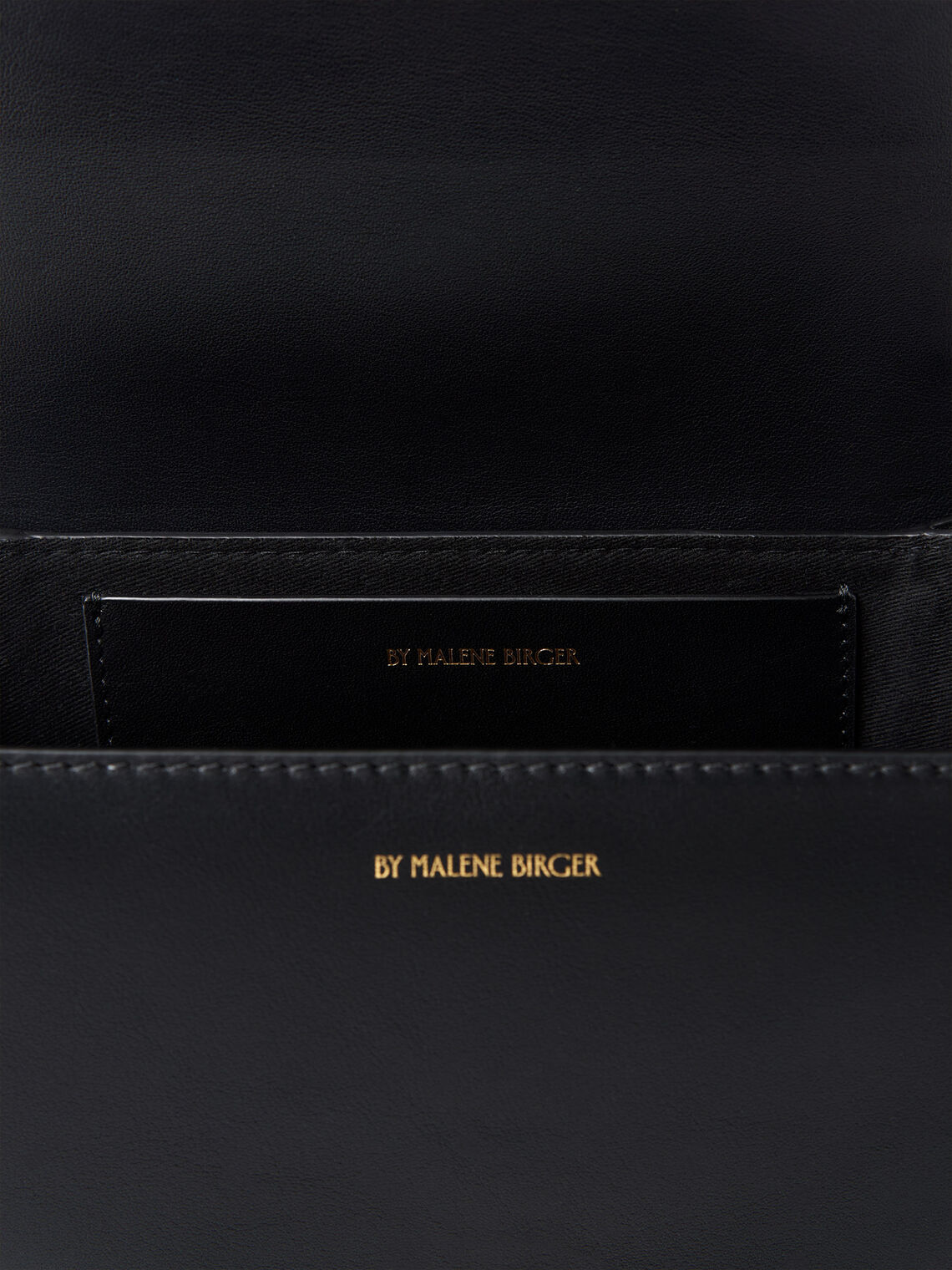 By Malene Birger Cebelle liten veske i sort kuskinn, med Swirl-motiv och justerbar axelrem.