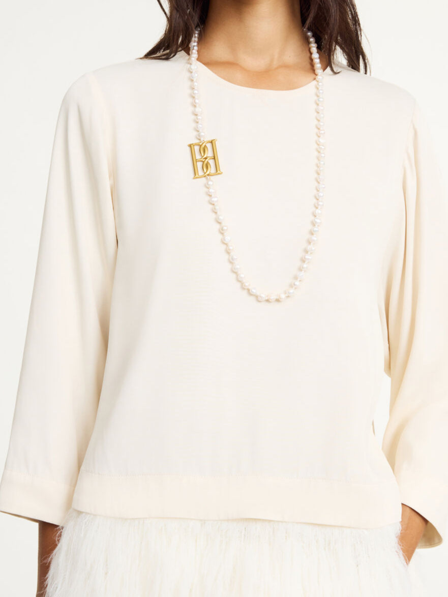 By Malene Birger Chakallo smykke i hvite ferskvannsperler med monogrambrosje, 89 cm langt.