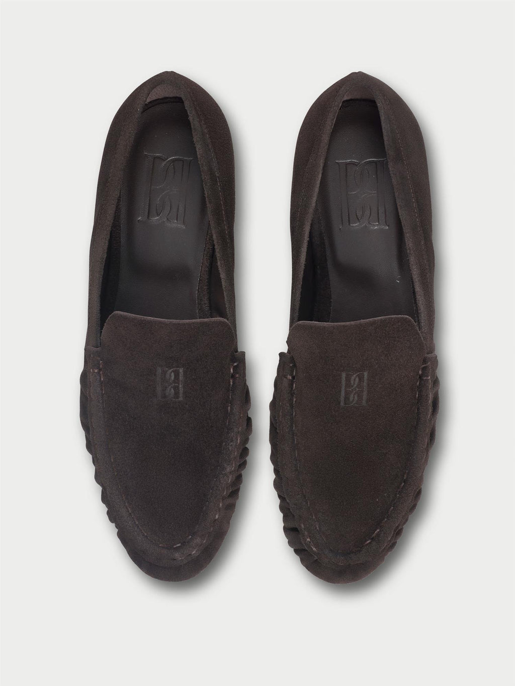 ELISA loafers fra By Malene Birger i fargen mørkebrun, laget i myk semsket skinn. Smal passform, rund tå og preget monogram over vristen.