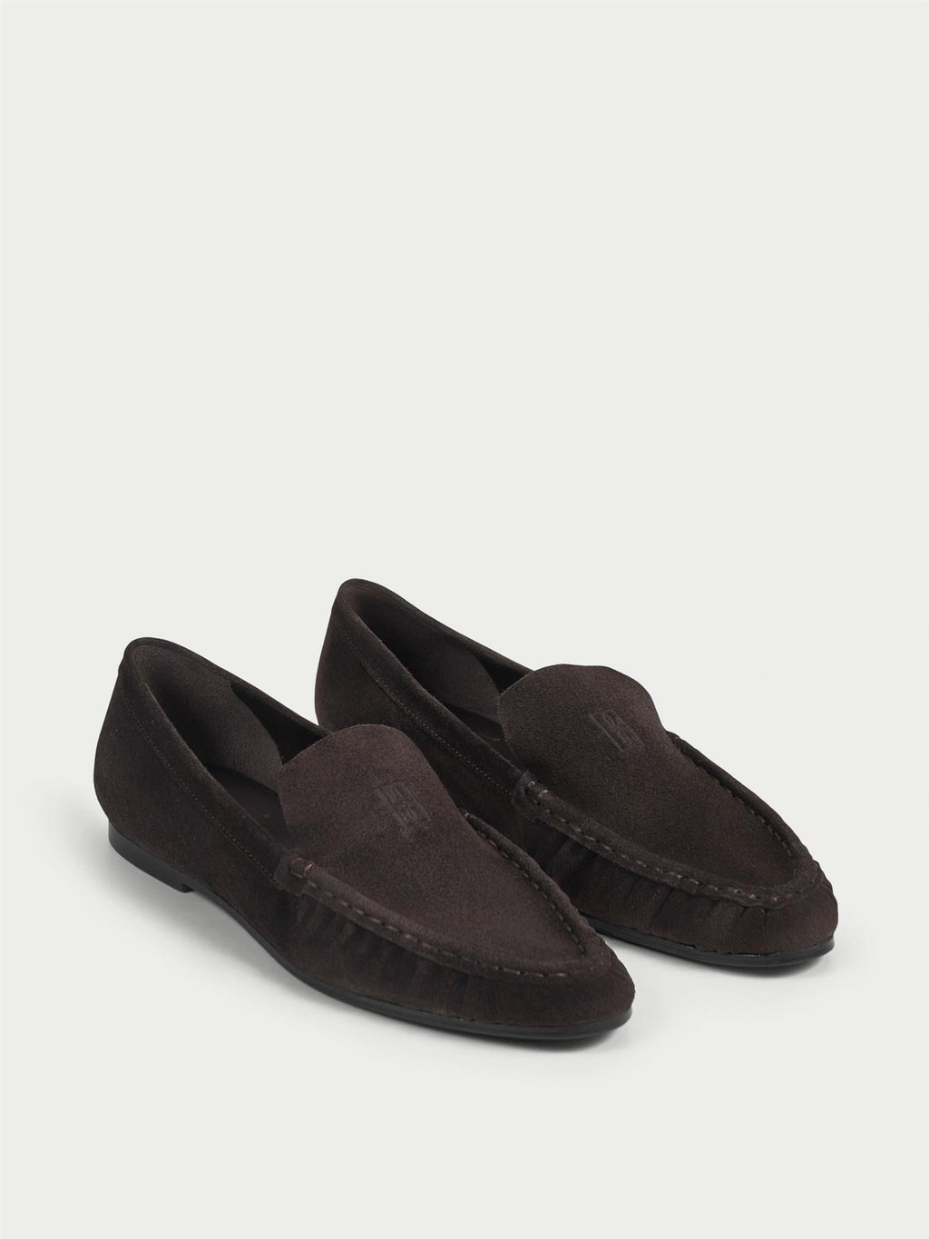 ELISA loafers fra By Malene Birger i fargen mørkebrun, laget i myk semsket skinn. Smal passform, rund tå og preget monogram over vristen.