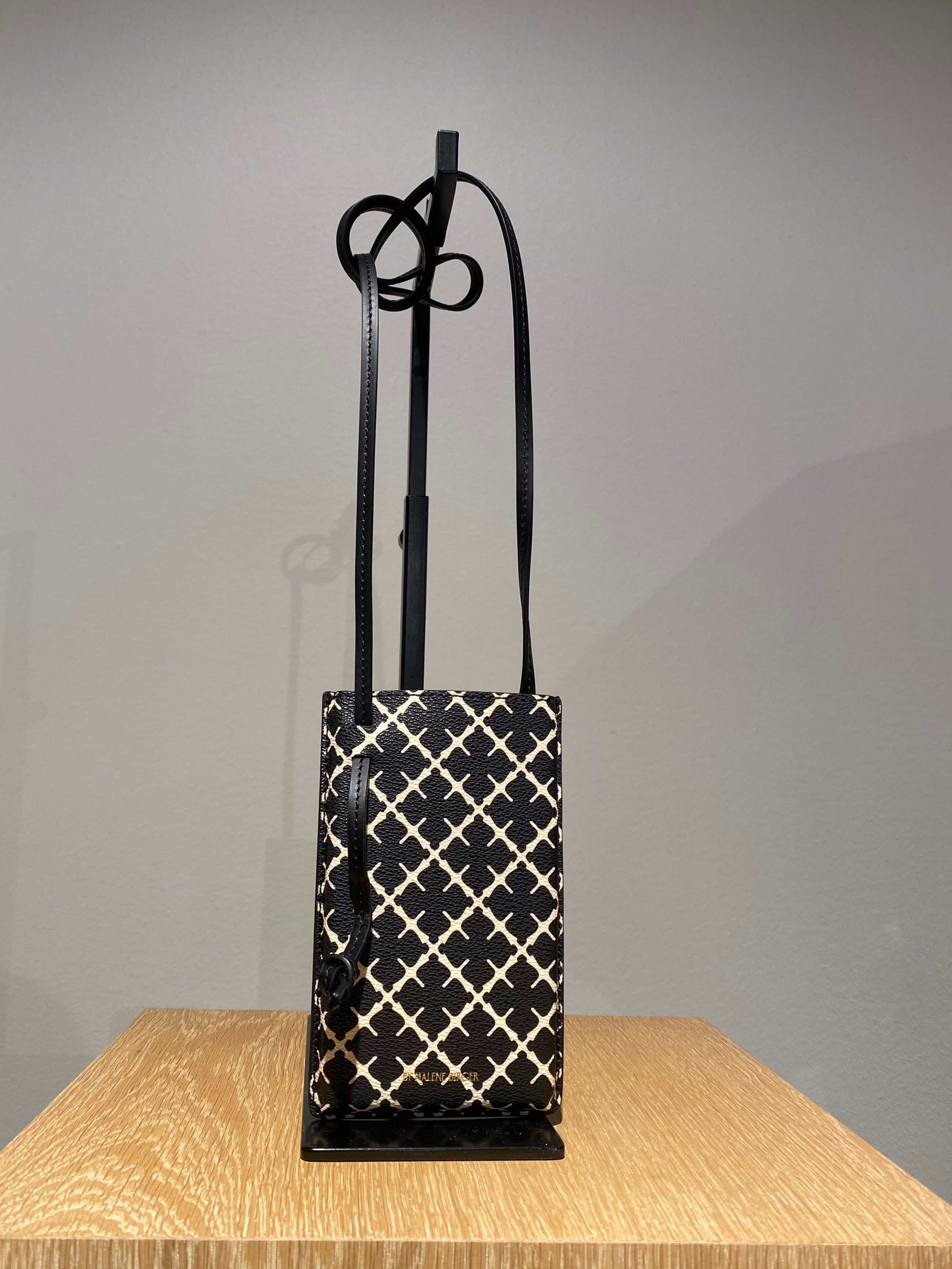 By Malene Birger Ivy mobilveske i sort polyvinyl chloride, med Signature Flower-mønster.