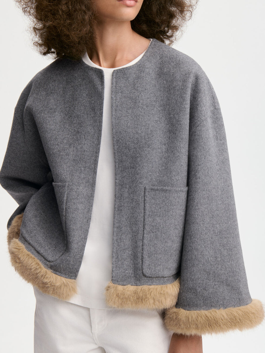 JACQUIELINE jakke fra By Malene Birger i fargen grå, laget i 100% ull med faux fur-avslutning på ermene og kroppen. U-foret med store lommer i front.