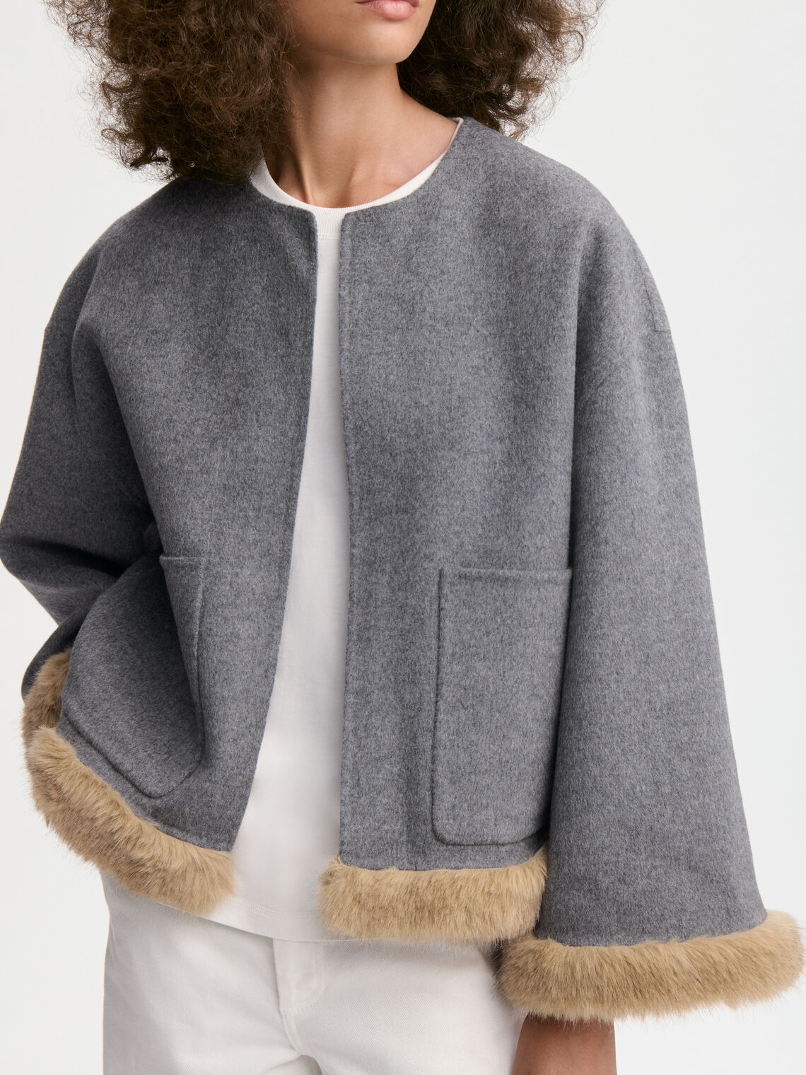 JACQUIELINE jakke fra By Malene Birger i fargen grå, laget i 100% ull med faux fur-avslutning på ermene og kroppen. U-foret med store lommer i front.