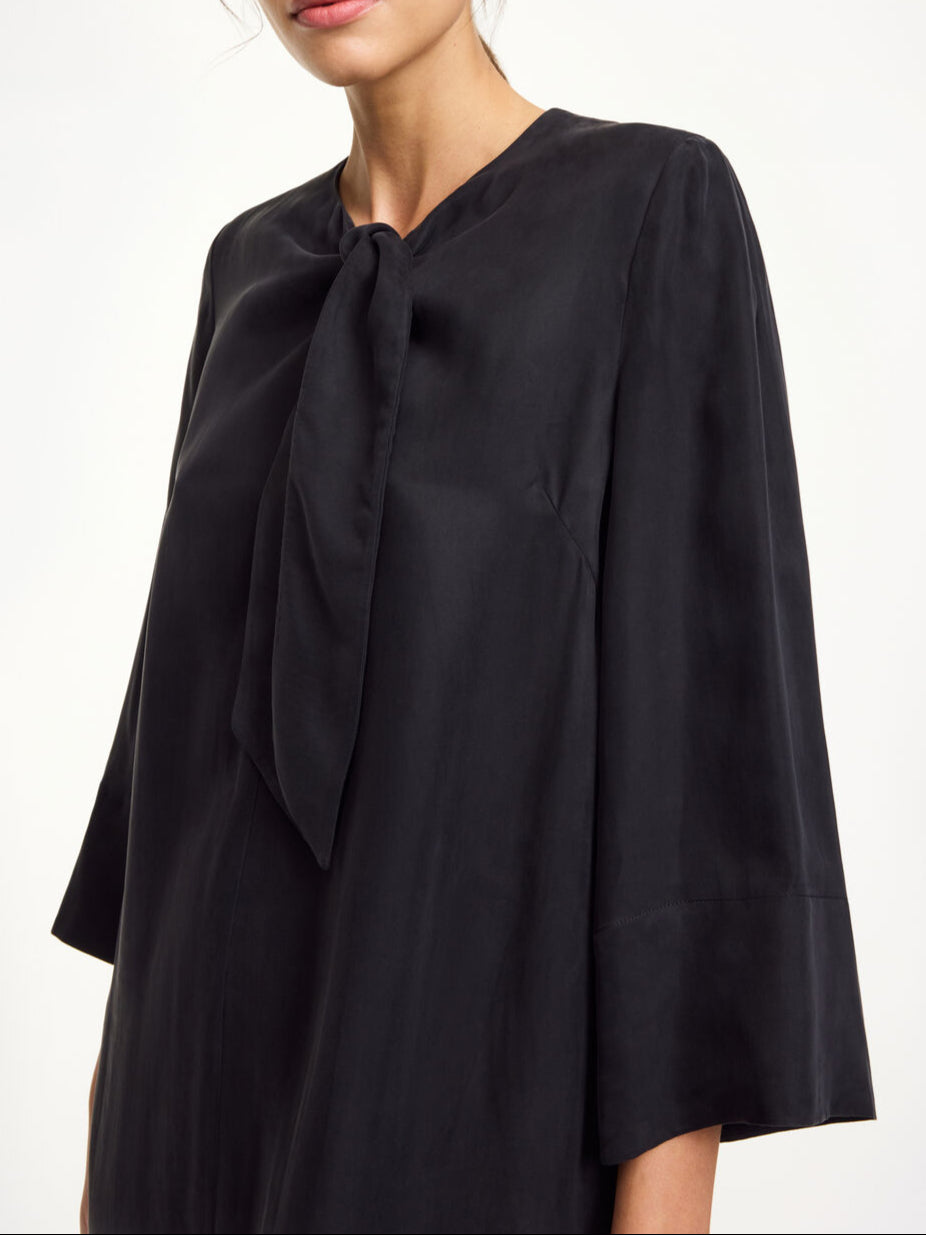 By Malene Birger Javea kjole i sort, med knyting i halsen, laget av en blanding av cupro og viskose.