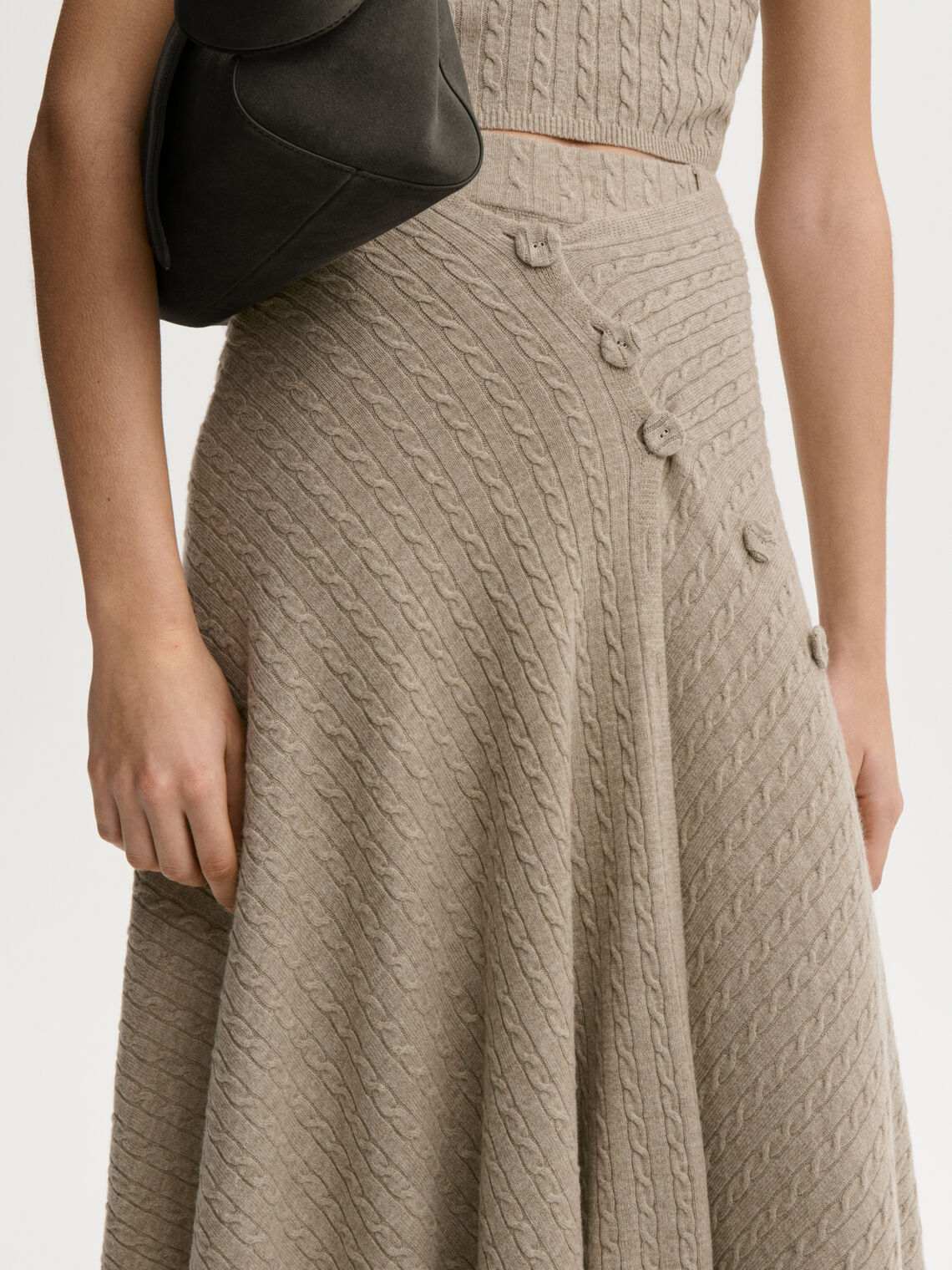 LIZA sjal/cape fra By Malene Birger i fargen beige, laget i 90% ull og 10% cashmere. Kabelstrikket og lukkes med trukne knapper – kan brukes som sjal over skuldrene eller som skjørt rundt livet.