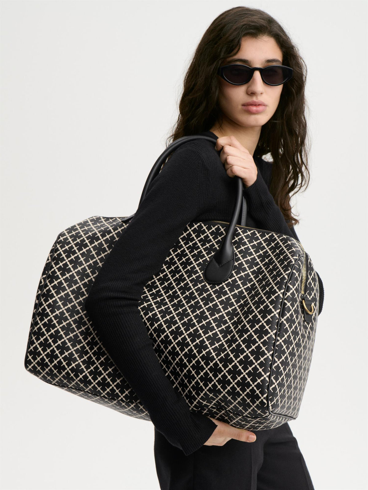 LULLU LARGE weekendbag fra By Malene Birger i fargen sort, laget i polyvinylklorid med Signatur Flower-print, avtagbar skulderreim og brede bærehåndtak.