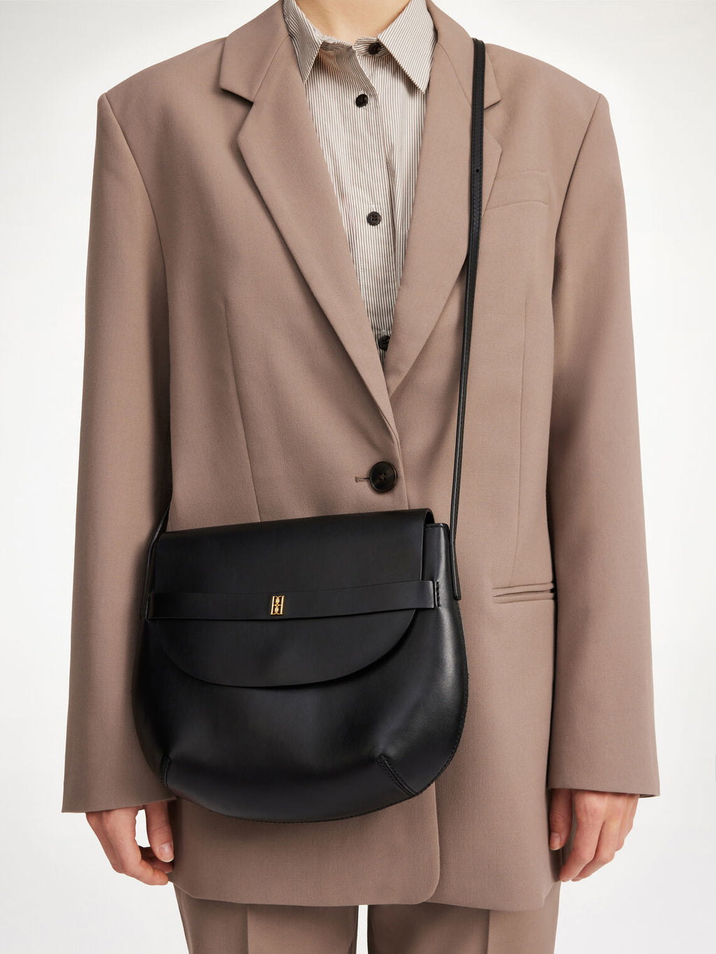 By Malene Birger Maellon veske i blankt, sort kuskinn, med diskret monogram i front og justerbar stropp.

