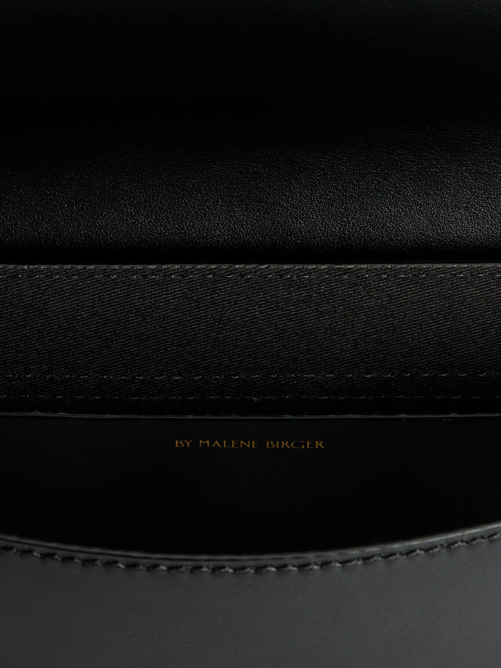 By Malene Birger Maellon veske i blankt, sort kuskinn, med diskret monogram i front og justerbar stropp.

