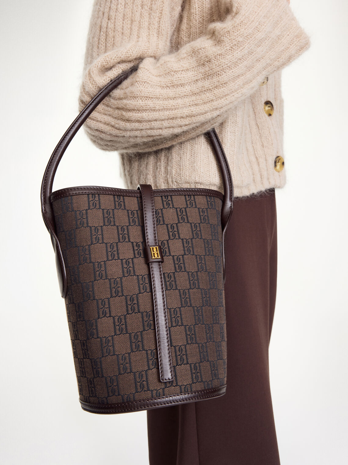 By Malene Birger Marylle bøtteveske i brun, laget av resirkulert bomull og polyester, med et gullfarget monogram-emblem i front.
