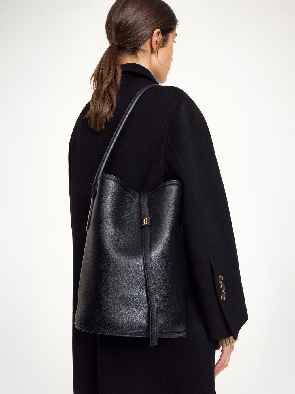 By Malene Birger Maryllon veske i sort skinn, med bøtteform og gullfarget monogram-emblem i front.