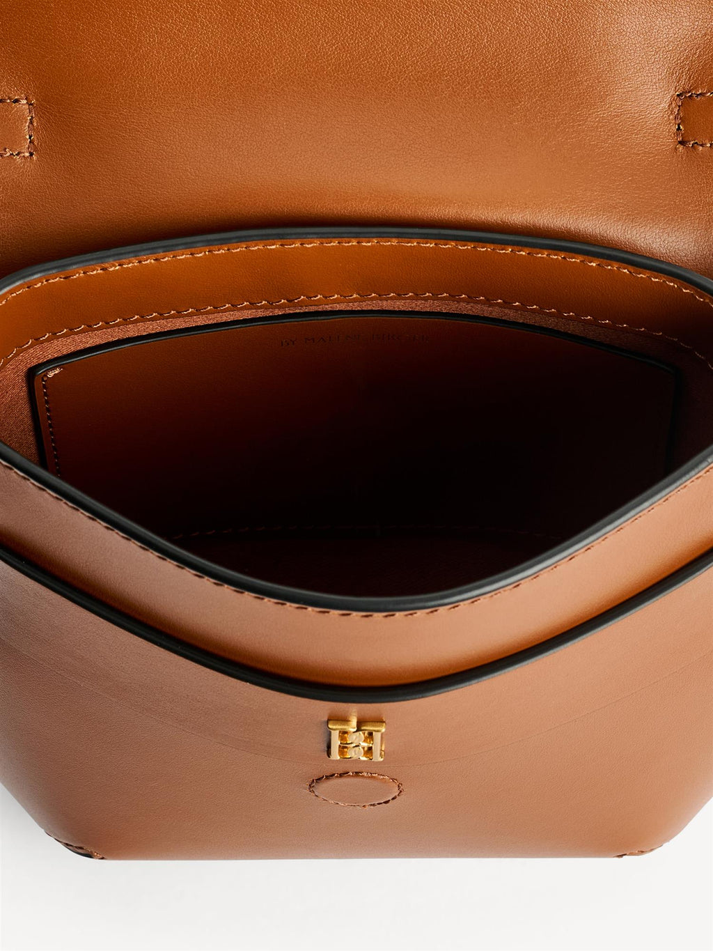 MEELA veske fra By Malene Birger i fargen brun, laget i 100% blank kuskinn. Liten, buet form med klaff og magnetlukking, justerbar stropp, bærehank og liten monogramdetalj i front.