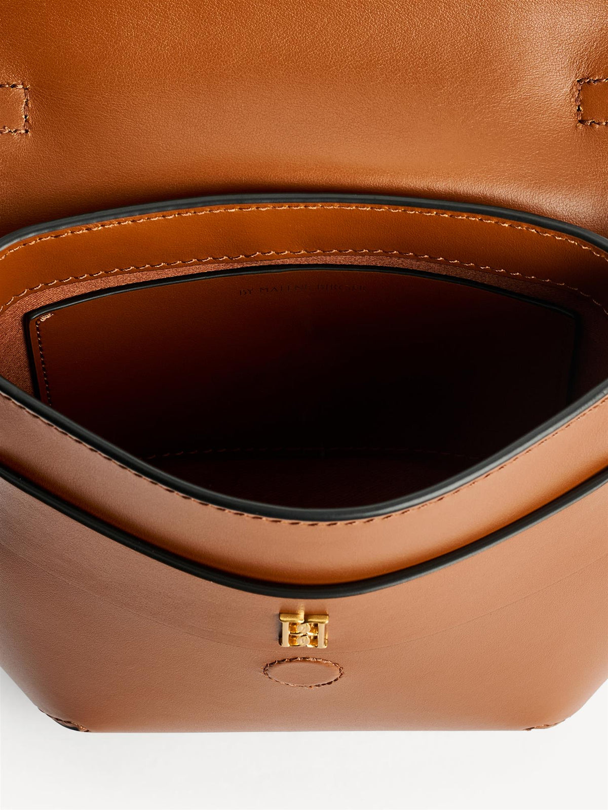 MEELA veske fra By Malene Birger i fargen brun, laget i 100% blank kuskinn. Liten, buet form med klaff og magnetlukking, justerbar stropp, bærehank og liten monogramdetalj i front.