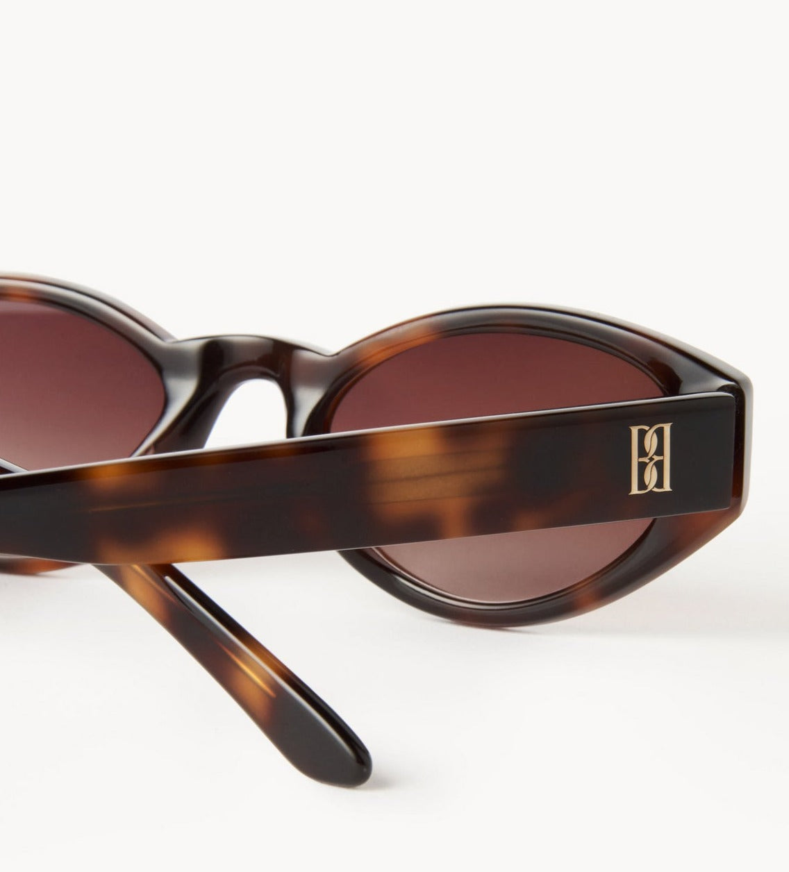 MYLA solbriller fra By Malene Birger i brun acetat med oval cat-eye ramme, mørke UV-beskyttende linser og monogram-emblem på siden.