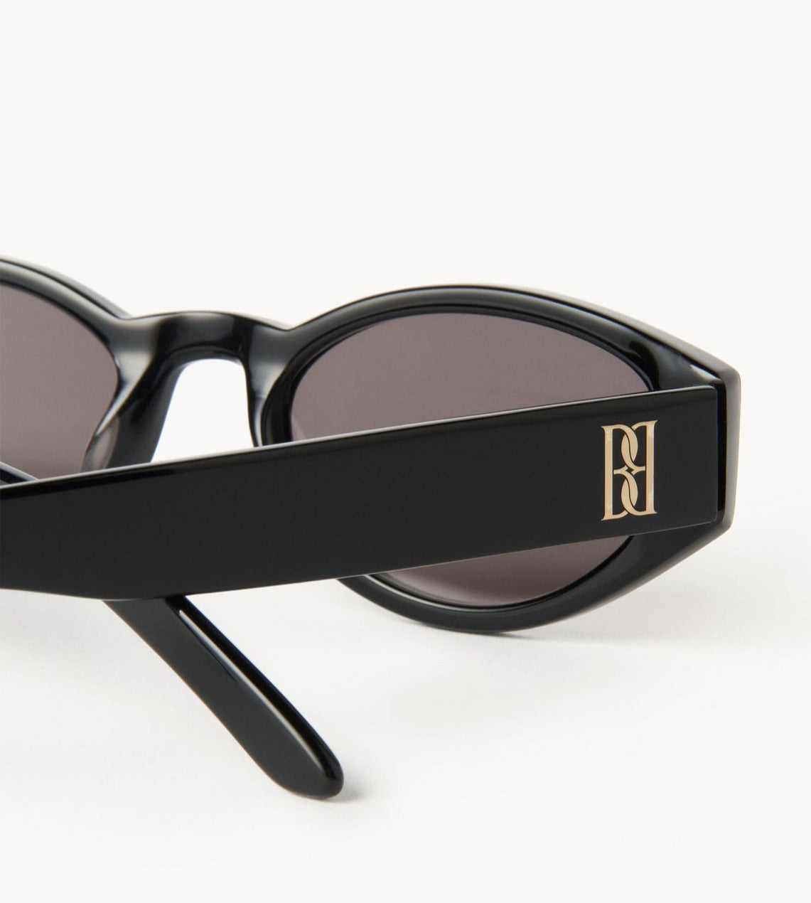 Sort oval cat-eye ramme i acetat, mørke UV-beskyttende linser, monogram-emblem på siden