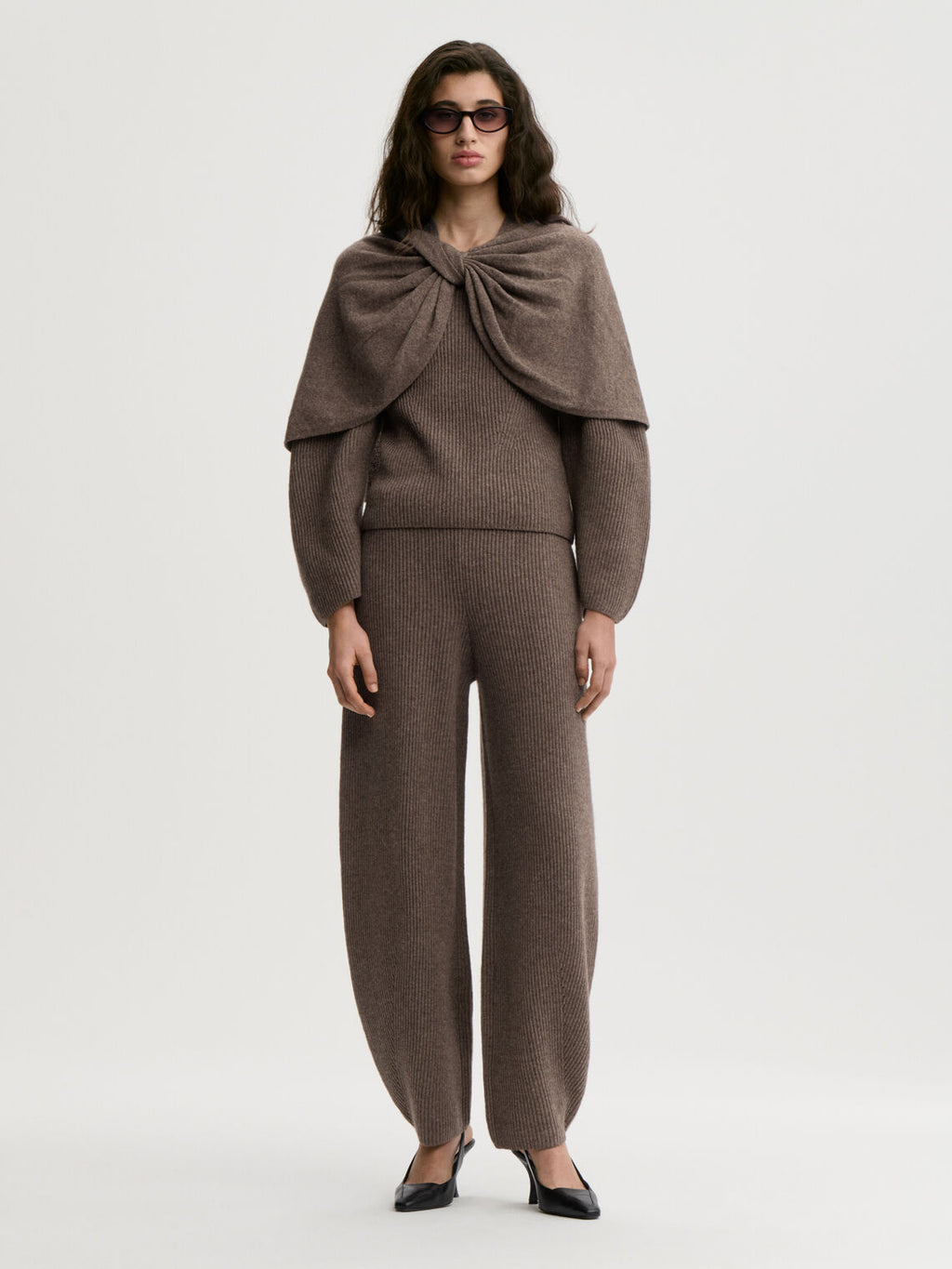 PINNE cape fra By Malene Birger i fargen brun, laget i 75% merinoull og 25% yak. Knytedetalj i front som kan brukes foran, på siden eller bak.