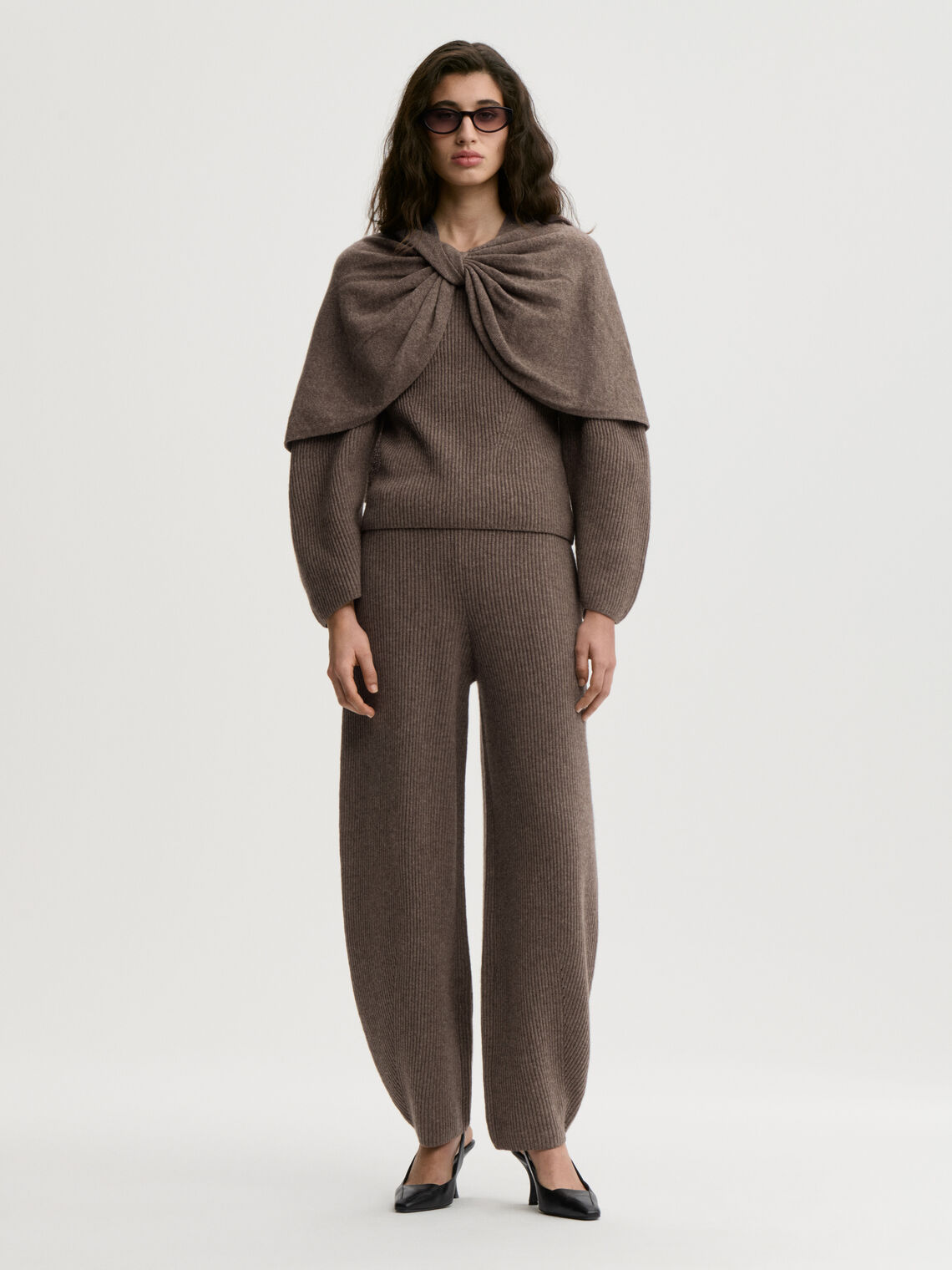 PINNE cape fra By Malene Birger i fargen brun, laget i 75% merinoull og 25% yak. Knytedetalj i front som kan brukes foran, på siden eller bak.