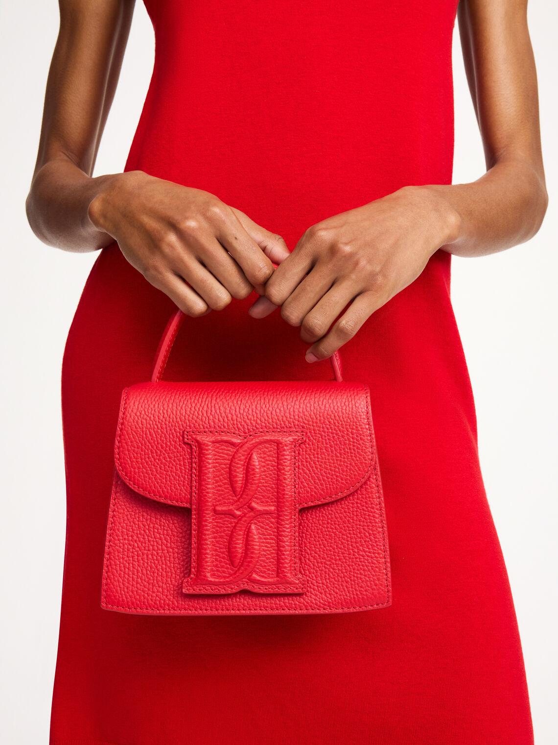 By Malene Birger Ramil veske i strukturert rød skinn, med monogram-motiv i front og justerbar skulderreim.