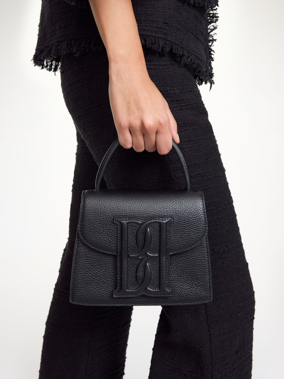 RAMIL veske fra By Malene Birger i fargen sort, laget i strukturert skinn med monogram-motiv i front og justerbar skulderreim.