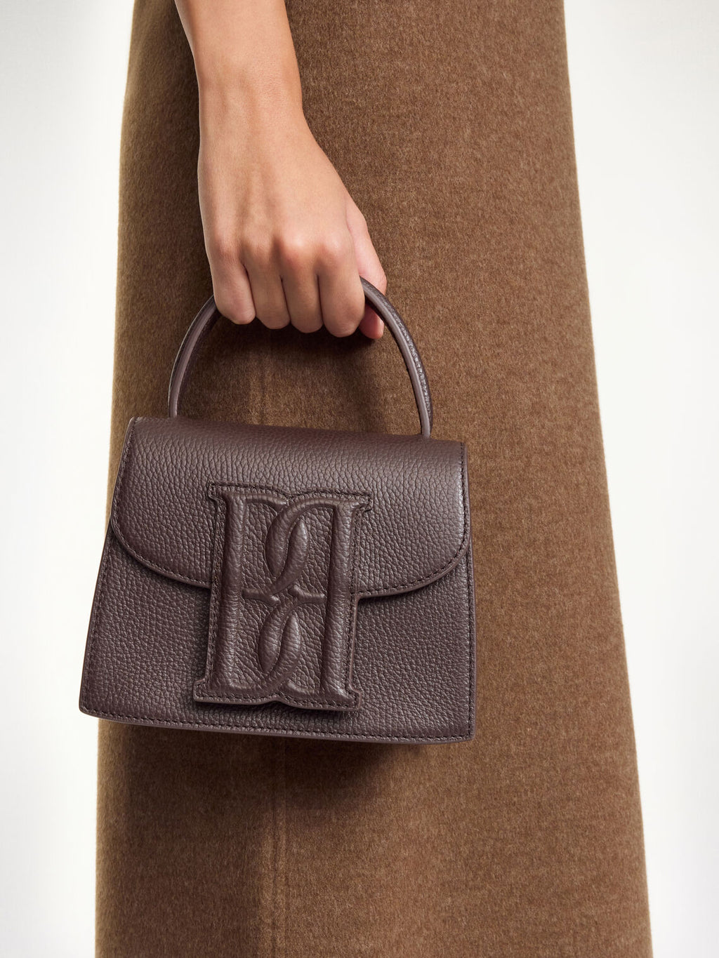 By Malene Birger Ramil veske i strukturert mørkebrun skinn, med monogram-motiv i front og justerbar skulderreim.