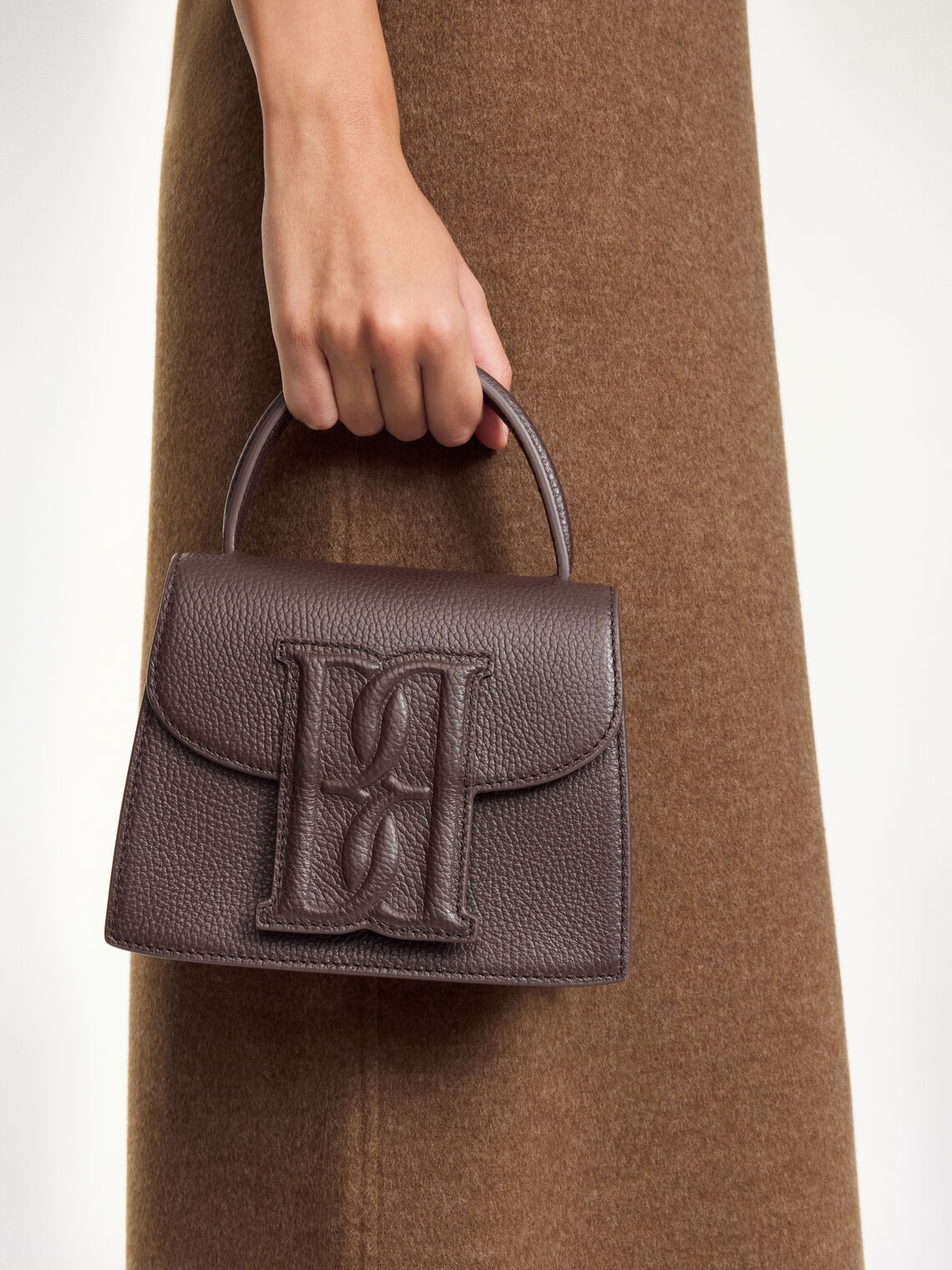 By Malene Birger Ramil veske i strukturert mørkebrun skinn, med monogram-motiv i front og justerbar skulderreim.