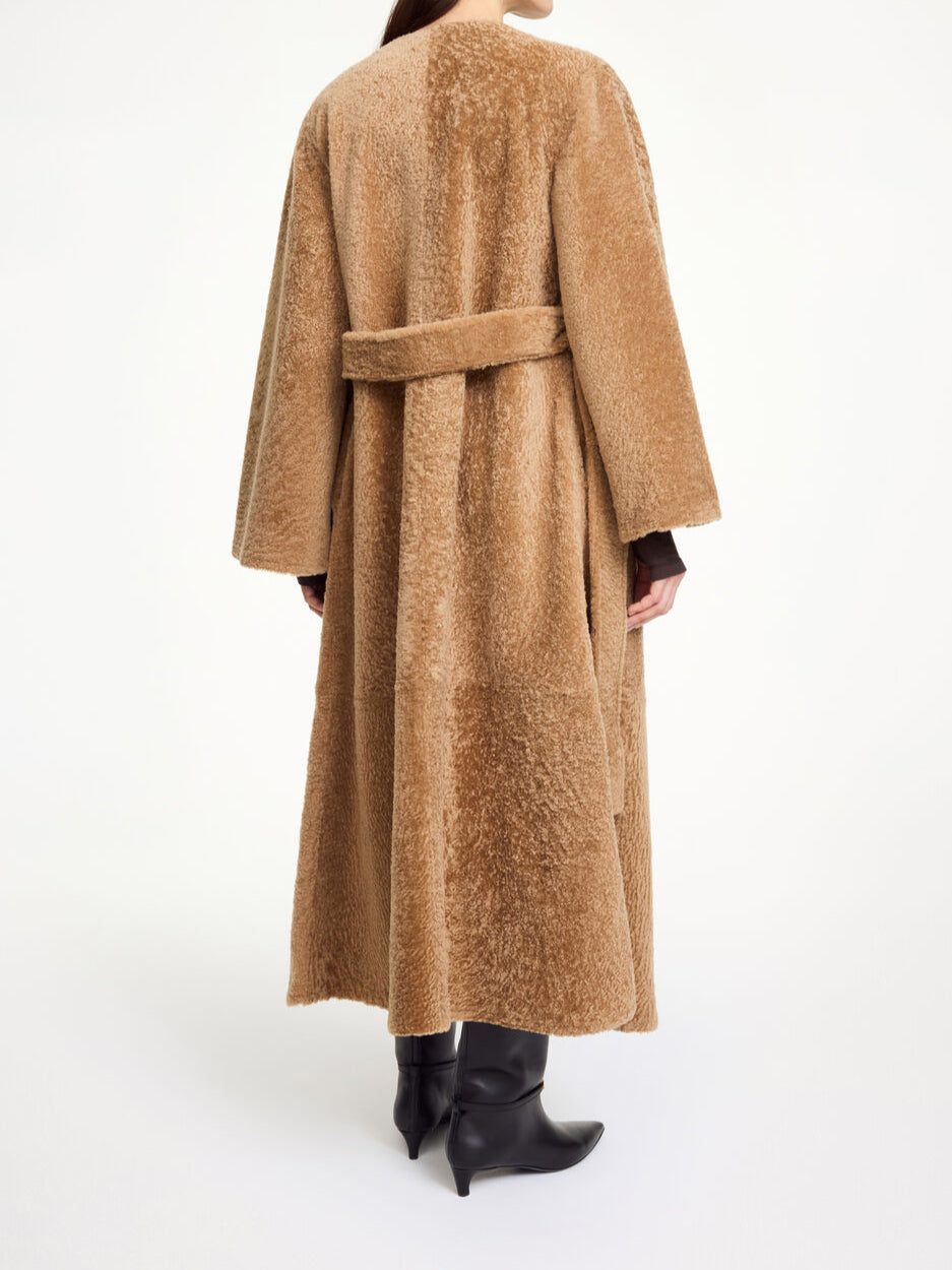 By Malene Birger Sandria lammeskinnskåpe i brun, laget av 100% lammeskinn og pels, med avtagbart belte og maksilengde.