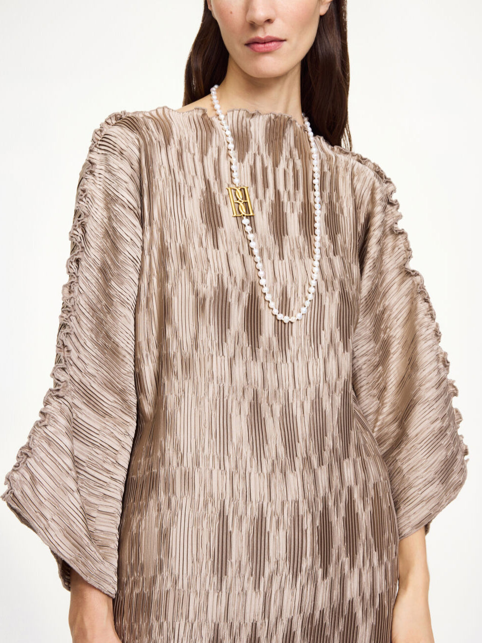 By Malene Birger Tralaido kjole i beige, med plissé struktur, båtutringning og vide ermer, laget av resirkulert polyester.