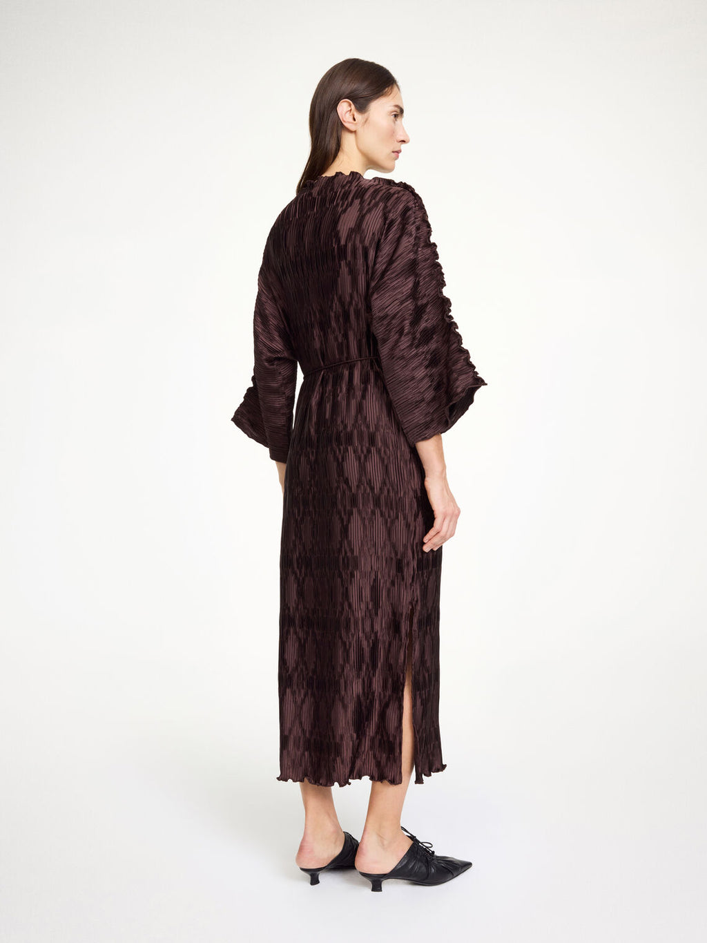 By Malene Birger Tralaido kjole i mørkebrun, med plissé struktur, båtutringning og vide ermer, laget av resirkulert polyester.