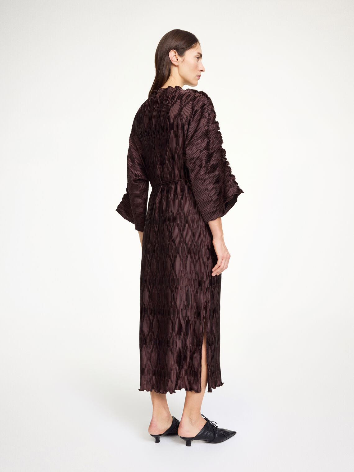 By Malene Birger Tralaido kjole i mørkebrun, med plissé struktur, båtutringning og vide ermer, laget av resirkulert polyester.
