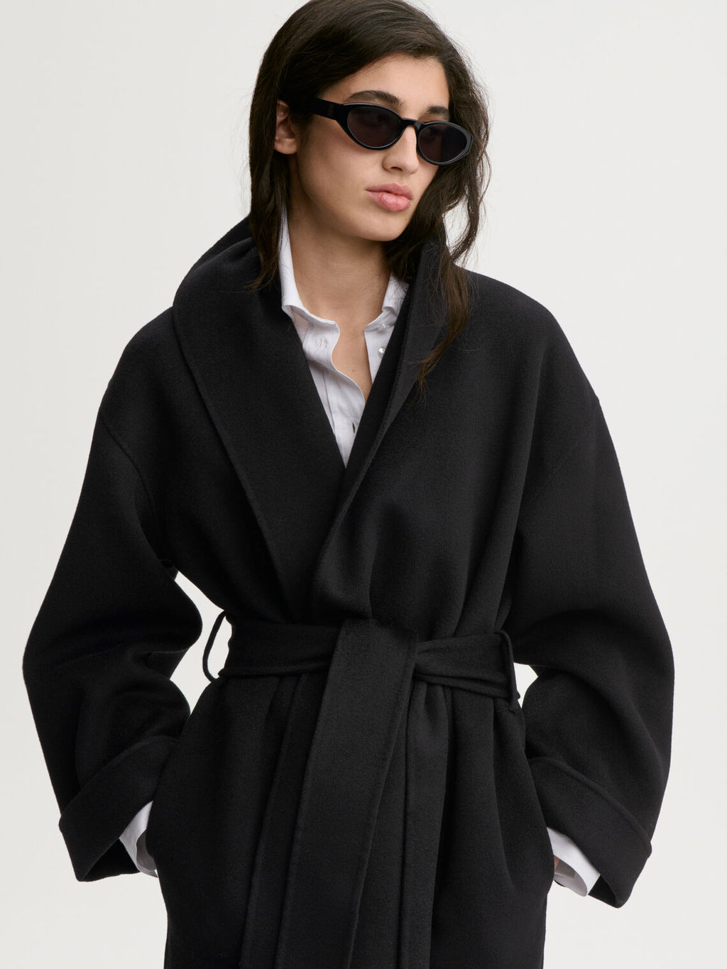 TRINELLE kort kåpe fra By Malene Birger i fargen sort, laget i 100% ull. Sjal-liknende krage/slag, rett i modellen og avtagbart belte.