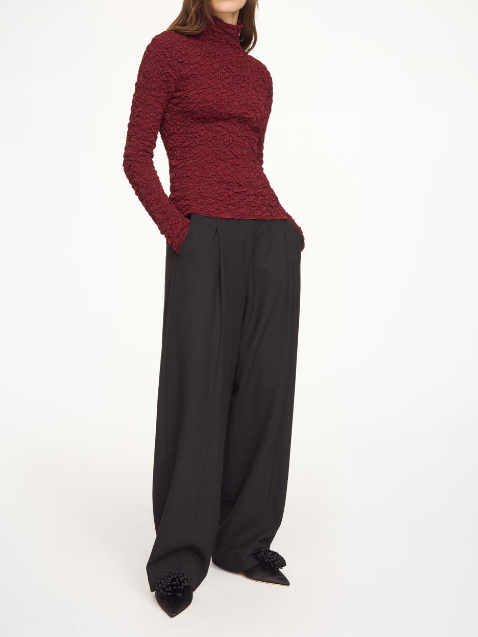 Lekker Aura-genser i fargen burgunder fra By Malene Birger med en stilfull struktur og elegant høy hals. Genseren har en smal passform som sitter tett etter kroppen, er laget i en noe gjennomsiktig og stretchy Lenzing Ecovero-viskose og har lange ermer som gir et dresset uttrykk.