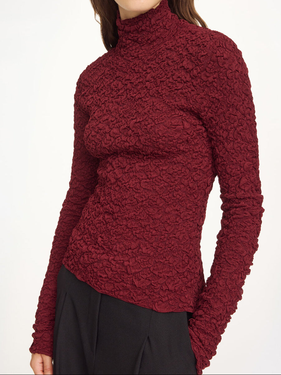 Lekker Aura-genser i fargen burgunder fra By Malene Birger med en stilfull struktur og elegant høy hals. Genseren har en smal passform som sitter tett etter kroppen, er laget i en noe gjennomsiktig og stretchy Lenzing Ecovero-viskose og har lange ermer som gir et dresset uttrykk.