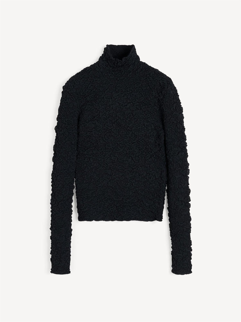 Aura-genser i fargen svart fra By Malene Birger med en stilfull struktur og elegant høy hals. Genseren har en smal passform som sitter tett etter kroppen, er laget i en noe gjennomsiktig og stretchy Lenzing Ecovero-viskose og har lange ermer som gir et dresset uttrykk.