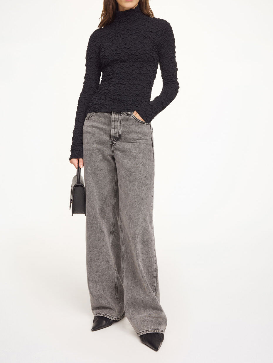 Aura-genser i fargen svart fra By Malene Birger med en stilfull struktur og elegant høy hals. Genseren har en smal passform som sitter tett etter kroppen, er laget i en noe gjennomsiktig og stretchy Lenzing Ecovero-viskose og har lange ermer som gir et dresset uttrykk.