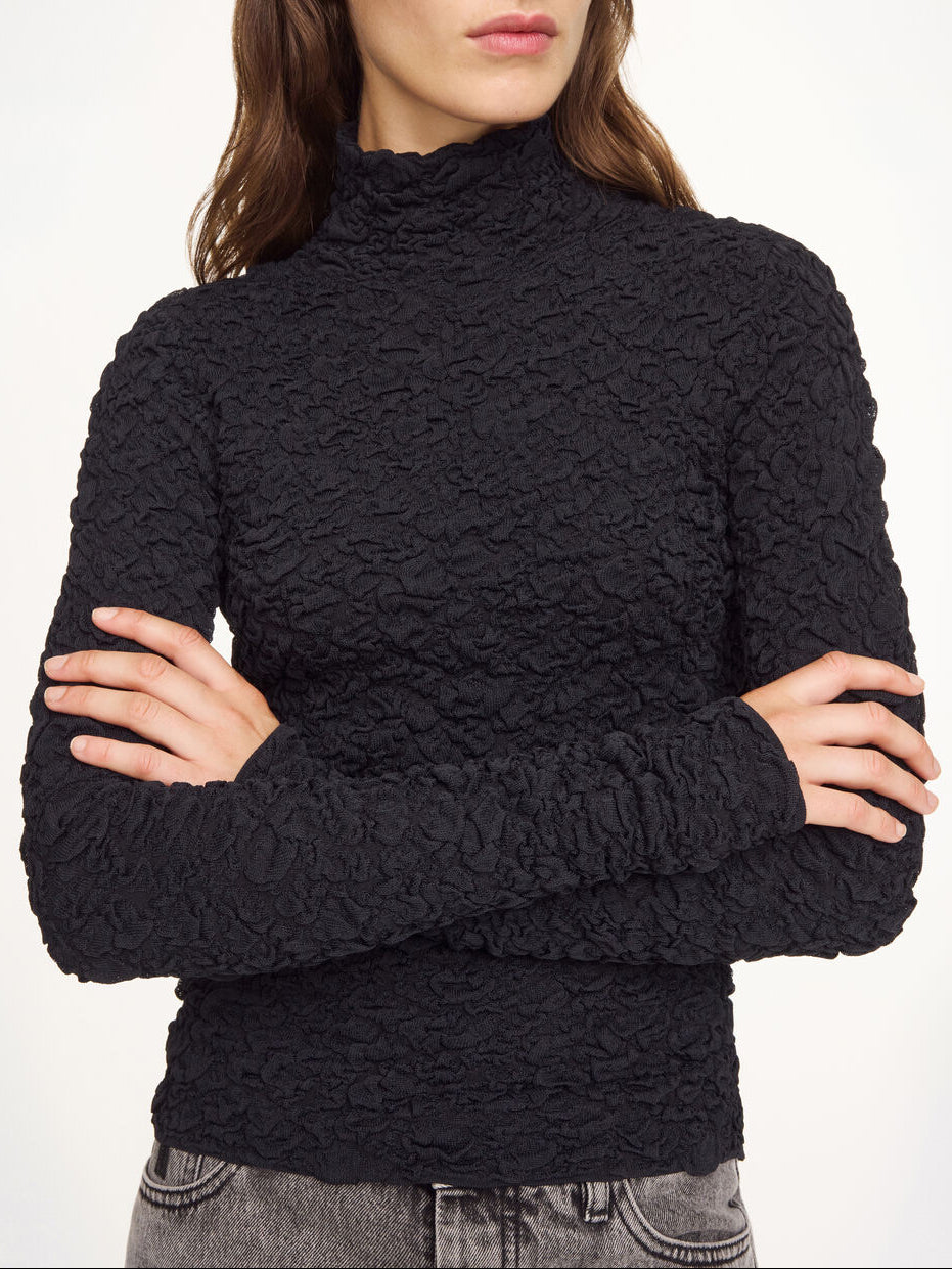 Aura-genser i fargen svart fra By Malene Birger med en stilfull struktur og elegant høy hals. Genseren har en smal passform som sitter tett etter kroppen, er laget i en noe gjennomsiktig og stretchy Lenzing Ecovero-viskose og har lange ermer som gir et dresset uttrykk.