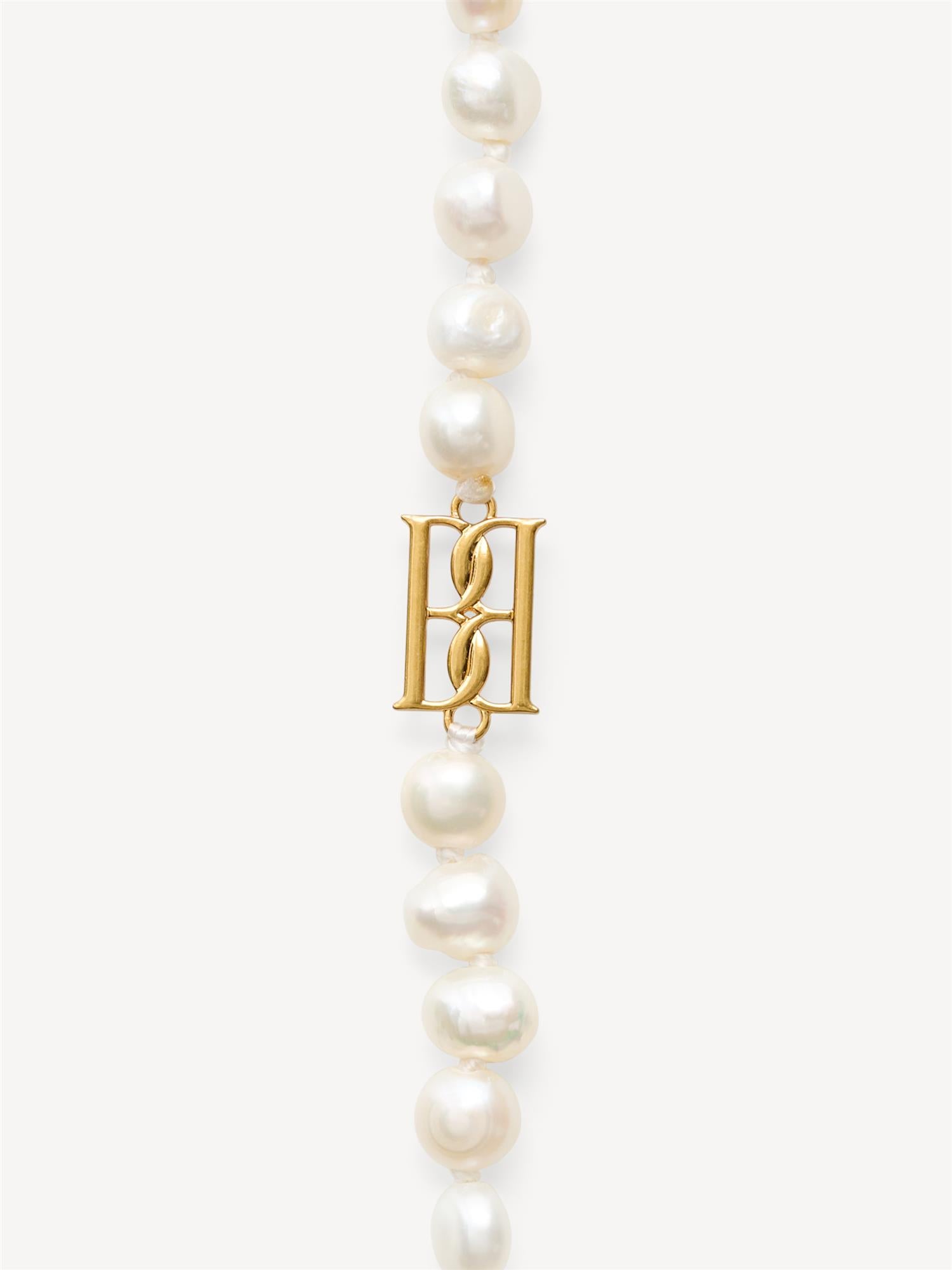 By Malene Birger Herlas fotlenke i hvite ferskvannsperler med monogram, 25 cm lang, lukkes med S-krok.