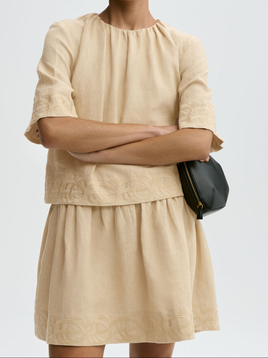 By Malene Birger Jania kjole i beige 100% lin med rund hals, knapplukking i nakken og swirl-broderi.