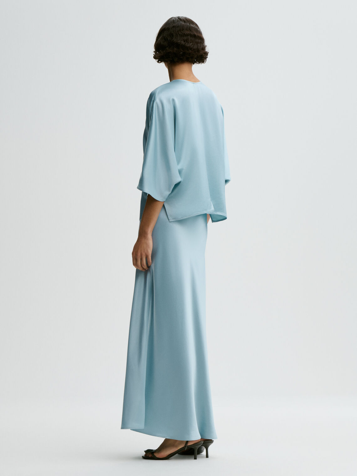 Lyseblå LUCIA satengbluse fra By Malene Birger, sett bakfra med flaggermus-ermer og draperinger.
