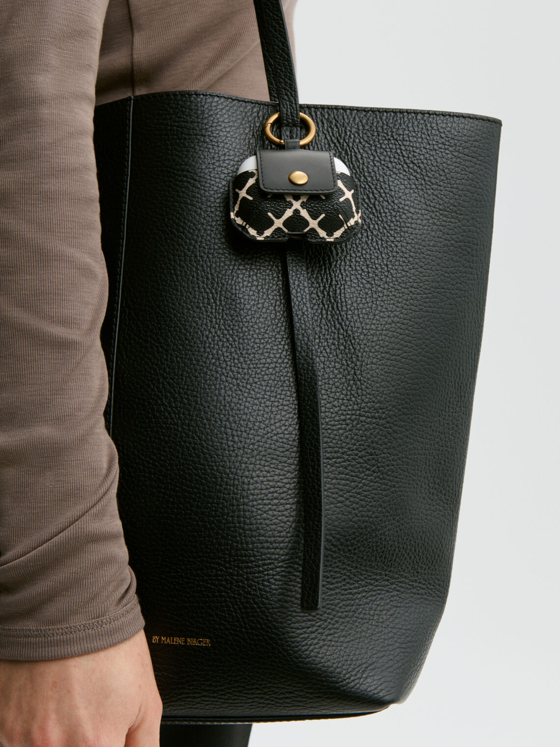 Lekkert ADA AirPod-etui i fargen sort fra By Malene Birger med det ikoniske Signature Flower-printet. Caset er designet for å kombineres med vesker eller nøkkelknipper, lukkes med en knapp i front og har en praktisk åpning for ladekabel i bunnen. Det er laget i et slitesterkt materiale og passer til AirPods av andre, tredje og fjerde generasjon.